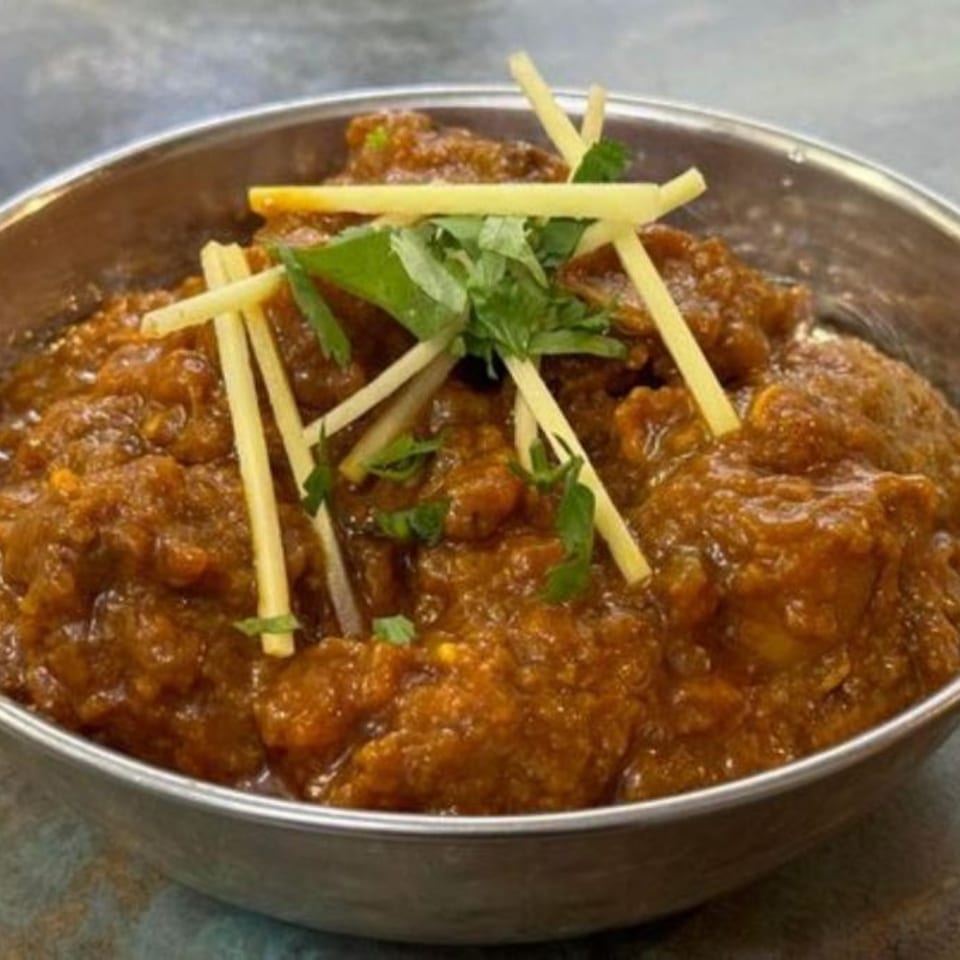 Rich brown curry in a metal bowl, garnished with julienned ginger and fresh cilantro.